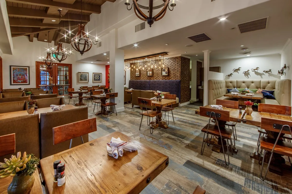 A warmly lit dining room featuring wooden tables, elegant chandeliers, tasteful artwork on the walls, and a plush seating area. The space exudes a cozy, inviting atmosphere perfect for family meals, social gatherings, or romantic dinners.