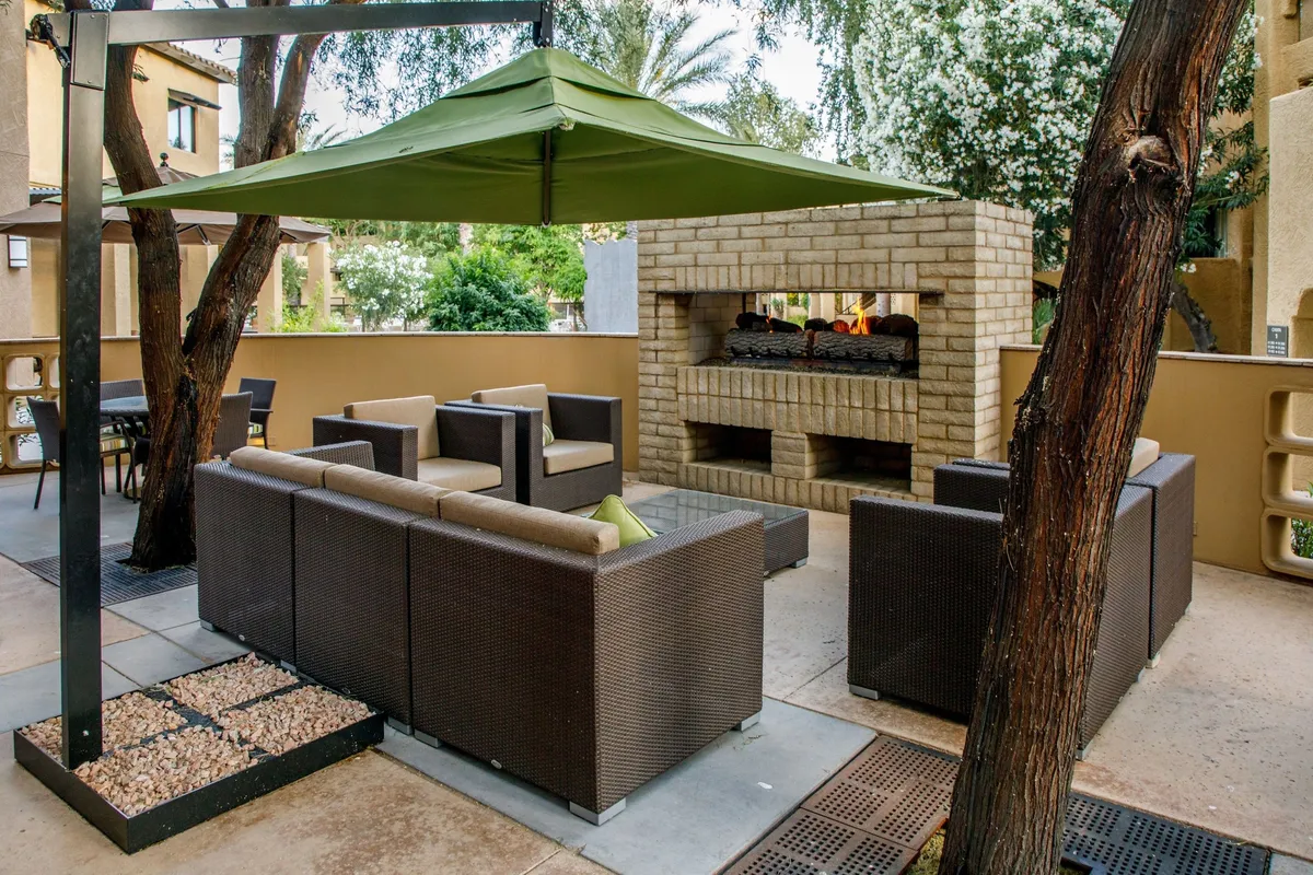 An inviting outdoor seating area beneath a lush green canopy, centered around a contemporary fireplace. Comfortable lounge chairs are arranged to foster conversation, while the fireplace promises warmth and ambiance. The scene is ideal for social gatherings or relaxing after a day on the golf course.
