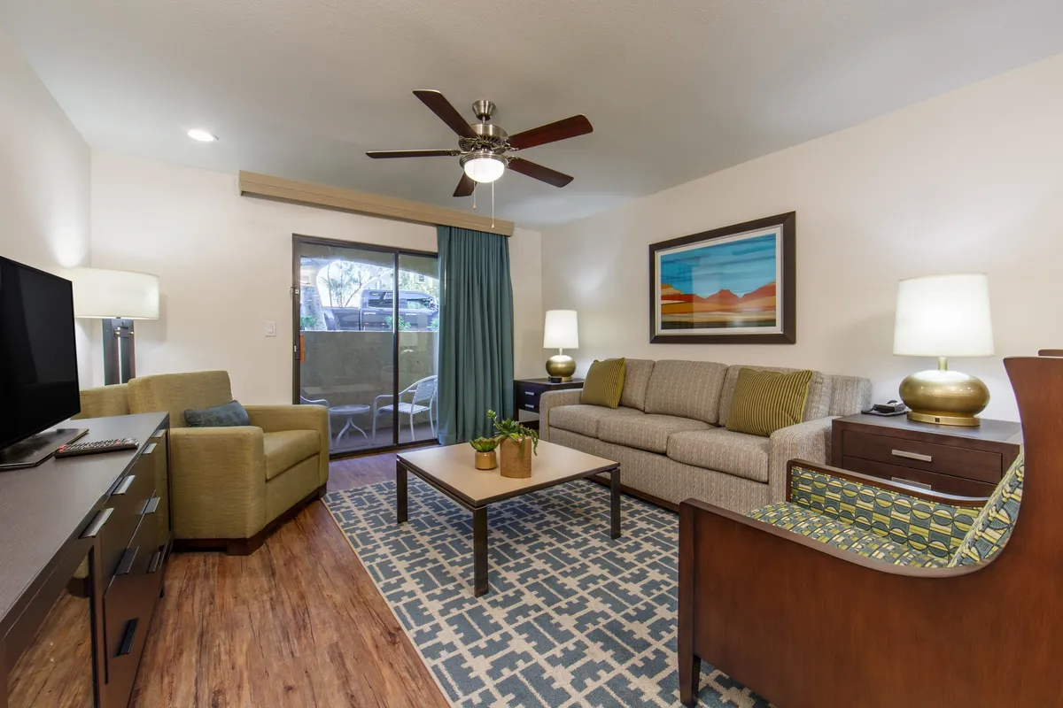 This image showcases a well-lit living room with a plush sofa, coffee table, armchair, television, and Southwestern-inspired artwork. The sunny atmosphere and inviting arrangement are ideal for relaxing, socializing, or enjoying a cozy movie night.
