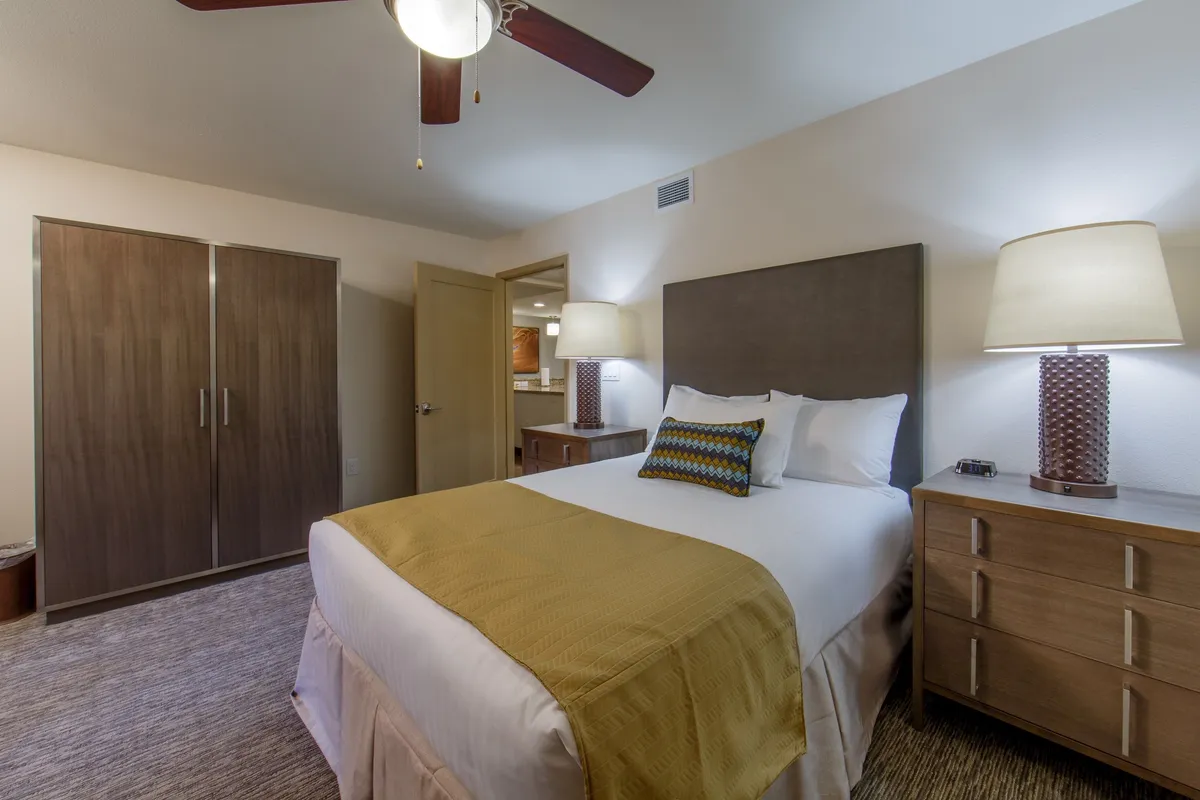 A serene bedroom scene featuring a comfortable bed adorned with decorative pillows, flanked by nightstands and lamps. The soft lighting and calm ambiance reflect a restful retreat, perfect for recharging after Scottsdale adventures.