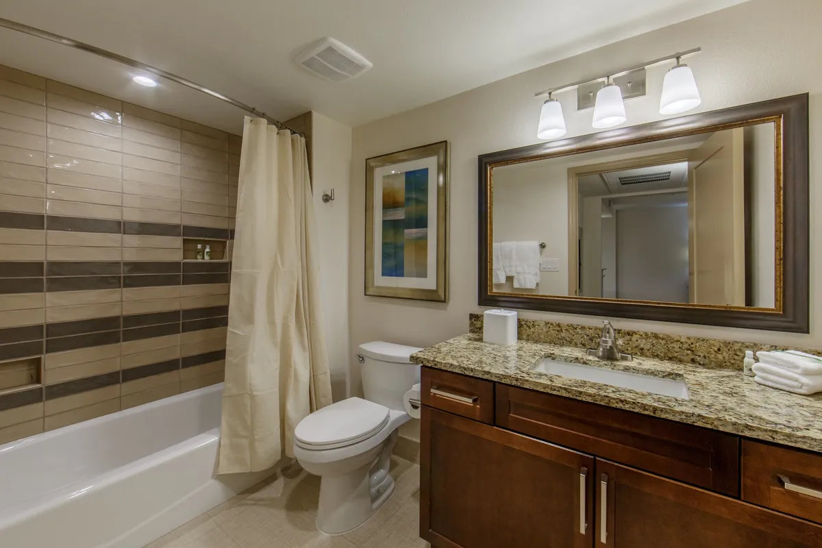 This bathroom features modern fixtures, a granite countertop, a textured tile wall, and framed artwork. The overall mood is tranquil and inviting, ideal for relaxing after a day of exploration or preparing for the next adventure.