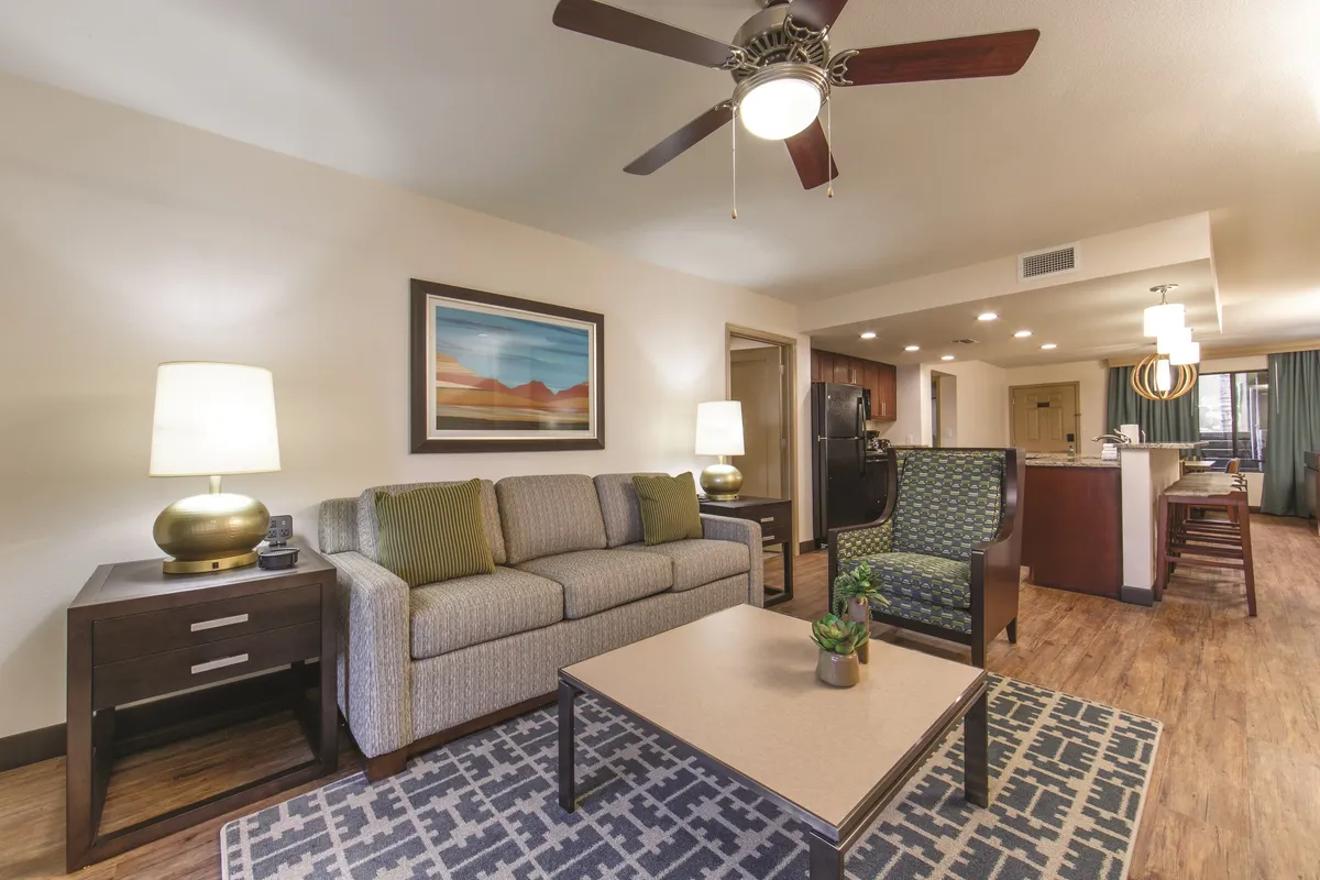 The image features a stylish and inviting open-concept living area with a comfortable sofa and coffee table, vibrant artwork on the walls, and a modern kitchen in the background. The space is filled with natural light, offering an ideal setting for relaxing, socializing, and entertaining. The scene evokes a sense of comfort and togetherness, perfect for families or friends.